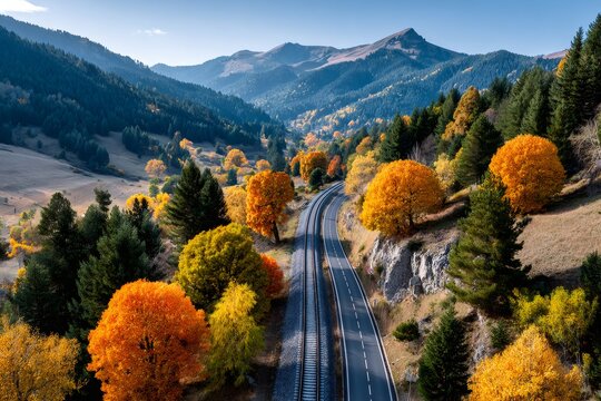 Mountain road and railway winding through autumn valley