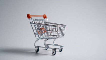 A small, empty miniature shopping cart with metallic frame and orange handles, isolated on a clean, light background, symbolizing retail or consumerism.