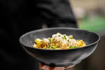 Delicious tortellini alla panna served in a black bowl. Hand holding gourmet Italian pasta with creamy sauce, parmesan cheese, and fresh parsley garnish. Close-up, nobody, shallow depth of field.