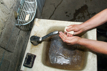 A stream of water flows from a mixer tap into a dirty sink where a person is washing their hands.