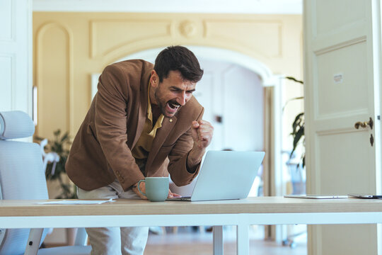 Confident Man Celebrates Victory At Office Desk With Laptop And Coffee