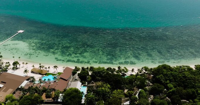 Emerald water and white sandy beach lined with palm trees and a beachfront resort. Rin Nai Beach. Ko Pha Ngan, Thailand.