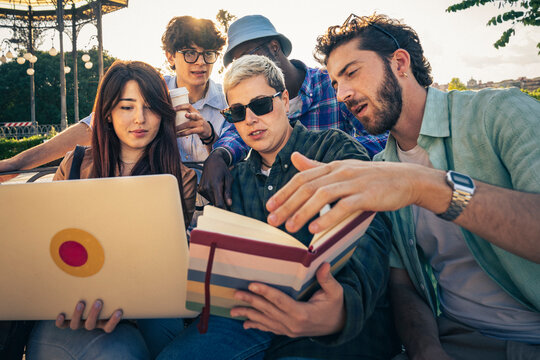 Group of friends collaborating on project using laptop and books outdoors