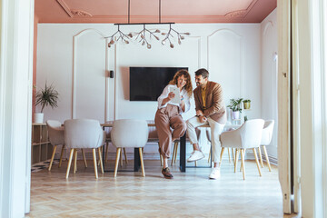 Young Couple Working and Laughing Together in a Modern Dining Room with Tablet