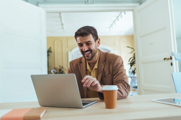 Happy Man Working on Laptop in Bright Office with Coffee Cup at Desk Today Morning