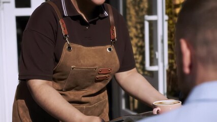 Over shoulder view of unrecognizable man sitting at cafe table and looking at unrecognizable waitress who holding tray with cup of coffee and dessert