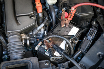 Two jumper cable clamps firmly attached to a vehicle battery inside the engine bay illustrates the jump starting process. Perfect for vehicle battery care, troubleshooting, and roadside support