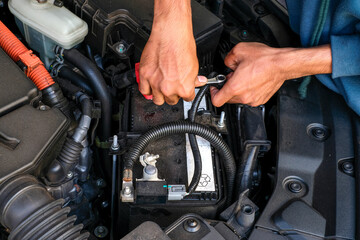 A mechanic replacing a car battery, tightening the terminal connection inside the engine bay. Perfect for vehicle maintenance, repair tutorials, automotive service, and battery replacement guides