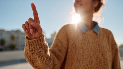 A young woman of Hispanic descent gestures upward with a finger while wearing a cozy sweater, illuminated by sunlight.
