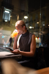 Woman drinking juice and using smartphone indoors