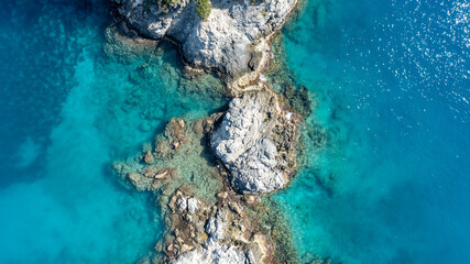 Top-down aerial view of dramatic cliffs meeting bright turquoise summer bays