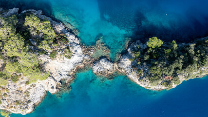Top-down aerial view of dramatic cliffs meeting bright turquoise summer bays
