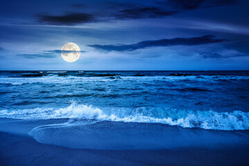 black sea waves crashing sandy beach at night. summer vacation on a windy weather under dark cloudy sky in full moon light. view of dramatic seascape. background for investment or abstract concepts