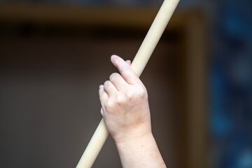 Elegant female hand holding a wooden gymnastics pole during practice in an apartment