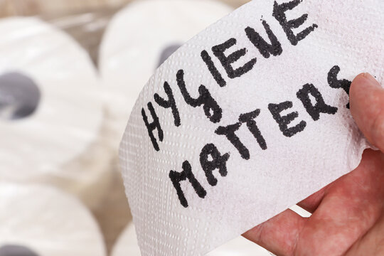 Hand holding a paper with handwritten text saying hygiene matters, surrounded by rolls of toilet paper. A reminder of the significance of cleanliness in daily life. - Powered by Adobe