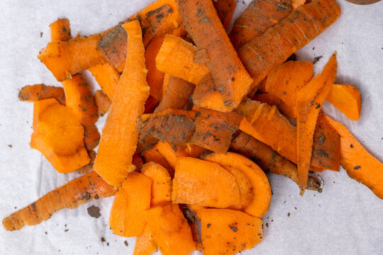 A pile of freshly peeled carrot scraps showcasing vibrant orange colors and earthy textures on a white surface. Ideal for culinary or sustainable lifestyle concepts. - Powered by Adobe
