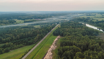 Aerial view of a serene landscape featuring lush forests and winding river under a cloudy sky. Captured in the evening, the scene showcases natures beauty and tranquility.
