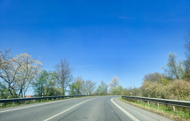 Curved road surrounded by trees under a clear blue sky, showcasing the beauty of nature in spring, ideal for travel and adventure themes.