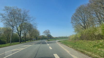 Fototapeta premium A scenic view of a curved road flanked by trees under a clear blue sky, providing a tranquil atmosphere ideal for travel or outdoor projects.