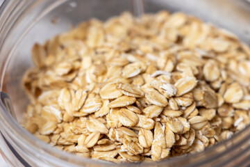 Close-up of whole oats in a clear glass jar. The raw, natural grains display a golden-brown color, suitable for healthy breakfast options or cooking recipes.