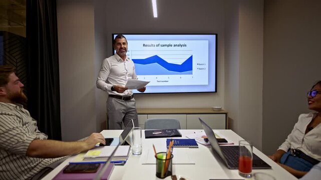An experienced businessman presents critical data analysis to a diverse team of professionals in a modern corporate meeting. - Powered by Adobe