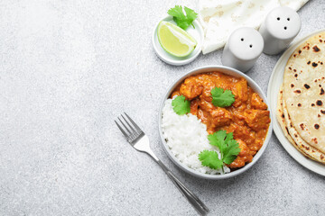 Delicious chicken tikka masala with rice, cilantro, lime and spices served on grey textured table, flat lay. Space for text