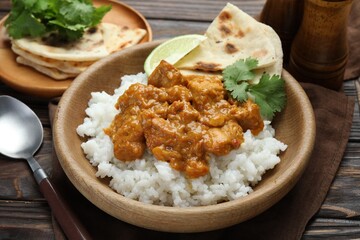 Delicious chicken tikka masala with rice, cilantro, lime and lavash in bowl on wooden table, closeup