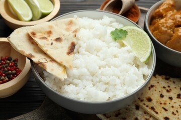 Delicious rice, cilantro, lime, lavash, chicken tikka masala and spices on wooden table, closeup