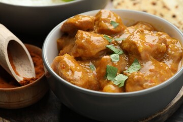 Delicious chicken tikka masala with cilantro and spices on table, closeup