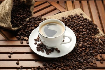 Aromatic coffee in cup and beans on wooden table