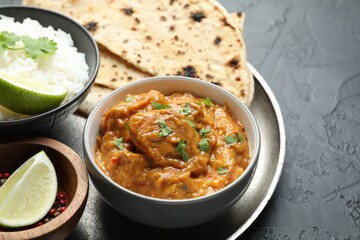 Delicious chicken tikka masala, lavash, cilantro, rice, lime and peppercorns on dark textured table, closeup. Space for text