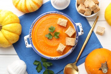 Tasty pumpkin cream soup with parsley, croutons, vegetables and shakers on white wooden table, flat lay
