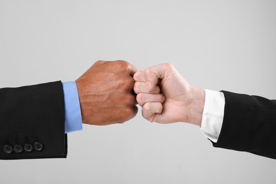 African American man bumping fists with his business partner on light grey background, closeup - Powered by Adobe