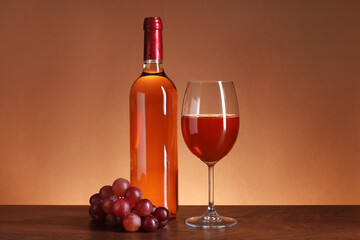 Rose wine in glass, bottle and grapes on wooden table against brown background