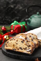 Traditional Christmas Stollen with icing sugar and festive decor on black table, closeup