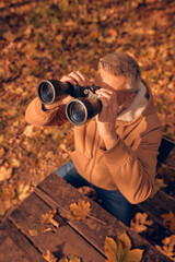 Amateur birdwatcher observing birds and other animals in nature with binoculars.