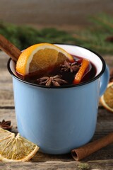 Tasty mulled wine in mug, spices and fir branches on wooden table, closeup
