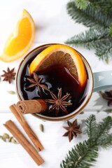 Tasty mulled wine in mug, spices and fir branches on white table, flat lay