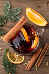 Tasty mulled wine with spices in glass cup and fir branches on wooden table, flat lay