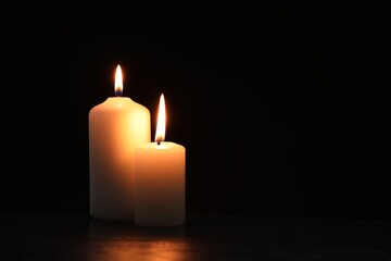 Beautiful candles burning on table against black background. Space for text