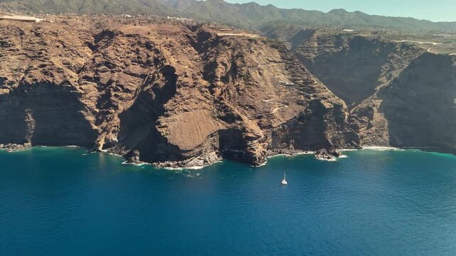 Aerial establishing shot of the hidden Por&iacute;s de Candelaria fishing village, revealing white houses built into the immense sea cliff on La Palma, Canary Islands, Spain.
