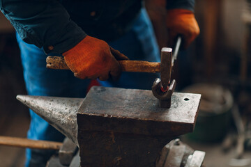 Blacksmith forges and making arrow metal detail with hammer and anvil at forge.