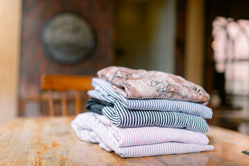 Freshly laundered shirts neatly folded on rustic wooden table evoke cozy home vibes, perfect for lifestyle blogs and relatable content with a touch of vintage charm
