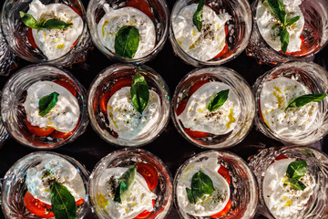 Top-down view of elegant crystal glasses filled with Caprese salad—sliced cherry tomatoes, burrata cheese, basil leaves, olive oil, and seasoning