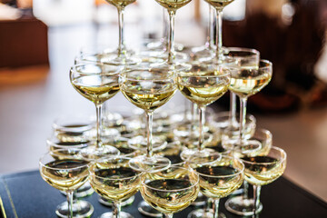 A structured champagne tower made of coupe glasses filled with white or sparkling wine, arranged on...