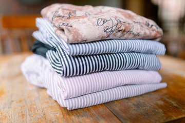 Stylish folded clothing stack on wooden table creates a chic, organized aesthetic for fashion blogs or home decor inspiration, showcasing modern stripes and elegant patterns
