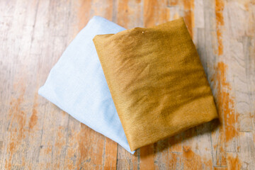 Two vibrant folded fabrics in light blue and golden brown on a rustic wooden surface create a warm and inviting textile design that's perfect for crafting projects