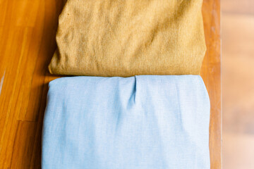 Soft folded fabrics in warm yellow and calming blue tones, perfect for textile design projects, sustainable fashion campaigns, or crafting inspiration on light wooden surface