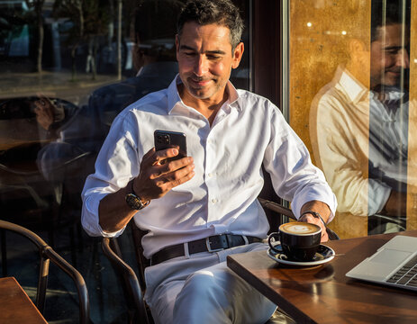 A businessman uses a smartphone while drinking coffee in a cafe.