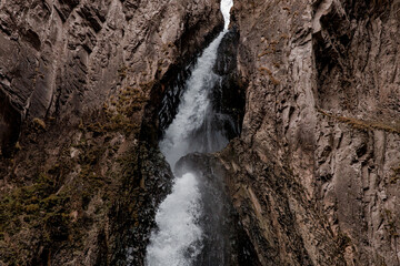Waterfall cascades down rocky cliffs in Kabardino-Balkaria. The surrounding landscape features rugged terrain and natural rock formations.